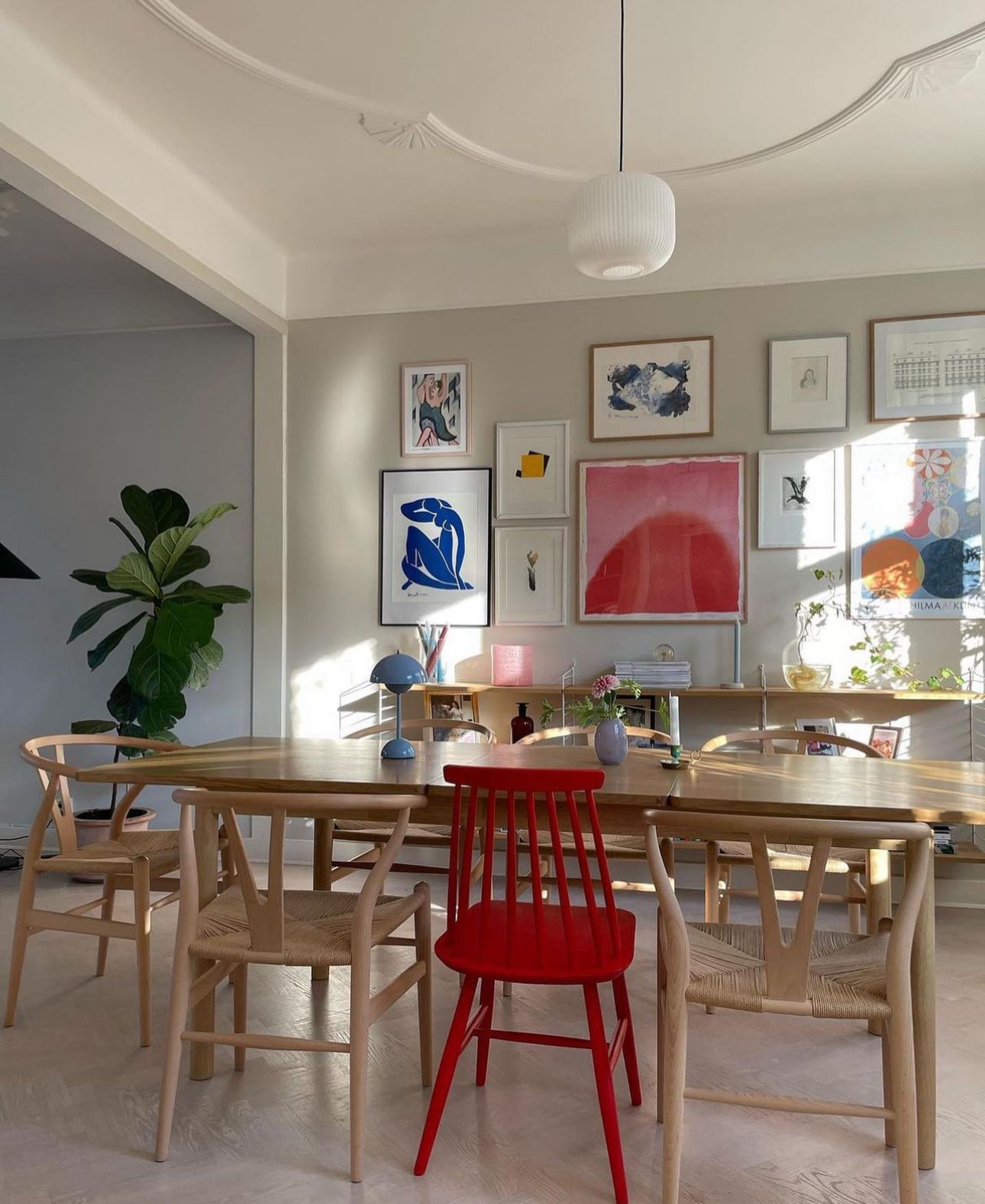 Scandinavian colorful dining room with different chairs, red accents and string shelves.
