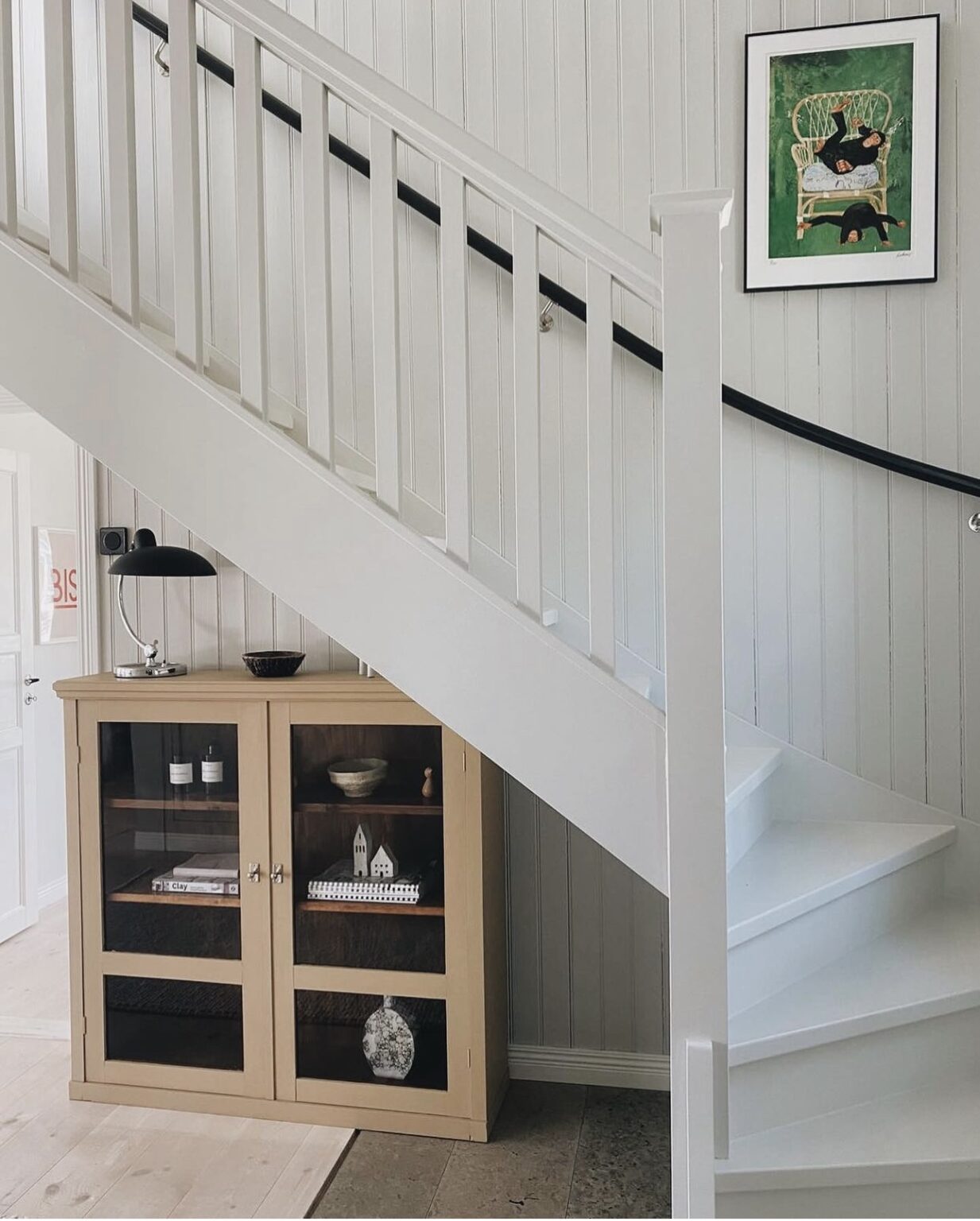 Light yellow glass door cabinet placed under a white staircase in scandinavian home