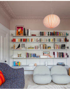 Scandinavian colorful living room with pink ceiling, striped lamp and big bookcase.