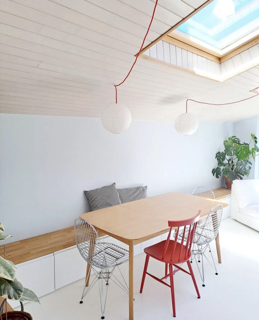 Light, bright and Scandinavian dining area with a ceiling window, red accent chair and storage bench.