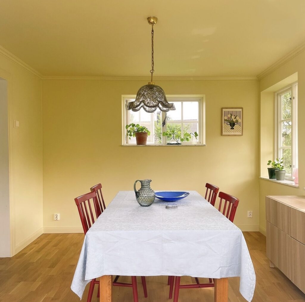 Yellow painted dining room painted with the color drenching technique. Paired with red chairs and antique lamp.