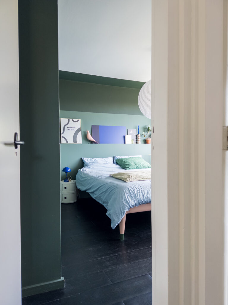 Green bedroom with black floors, white ceiling and colorful details.